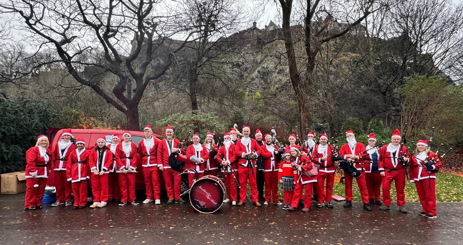 Stockbridge Pipe Band members in Santa suits at the When You Wish Upon a Star Santa Stroll